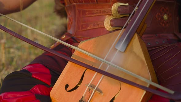 Musician in Ethnic Leather Clothes Plays Igil on Field