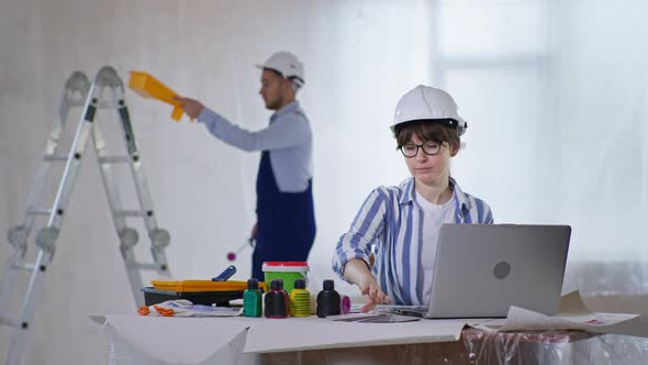 Woman in Safety Helmet Smiles and Enjoys Choosing Paint Color on a Color Palette for New Walls at a