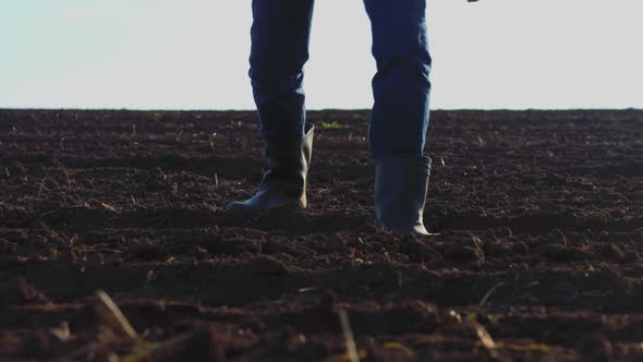 Close Up Farmer in Rubber Boots Walks on the Surface of the Rich Soil
