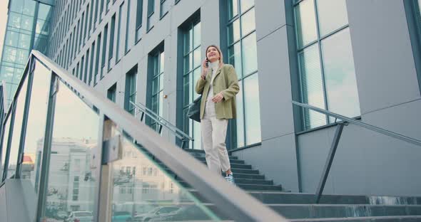 Woman Walking Down the Stairs Speaking on Mobile Phone Background of a Modern Business Center.