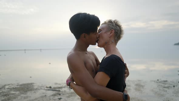 Hugging Couple with Age Differences Kissing on a Beach and an Look at Camera at Seaside Sunset Face