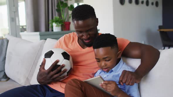 African american father and son cheering together while watching sports on digital tablet at home