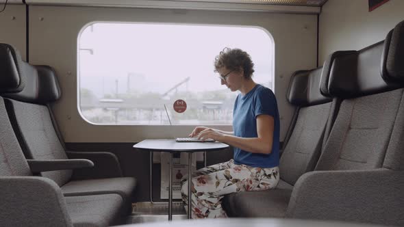 Woman in Glasses Working on a Laptop While Going By Train