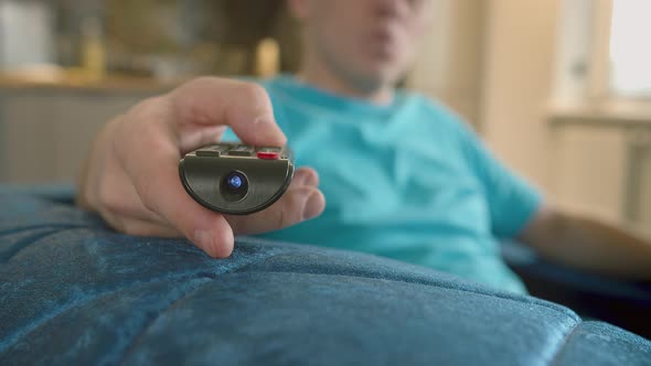 Closeup of a Man's Hand with a Television Remote Control Sitting at Home on the Couch