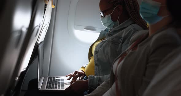 African senior woman sitting inside airplane and using computer laptop