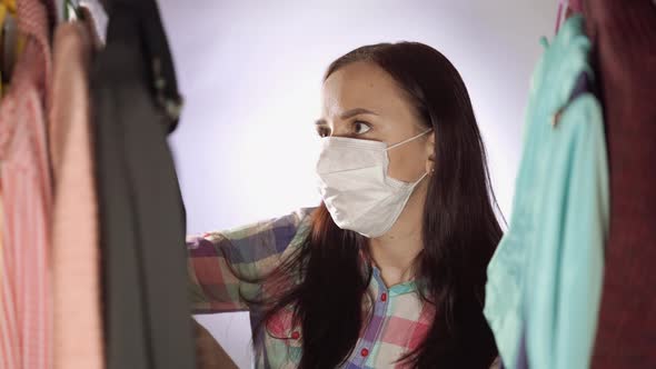 Close Up of Young Woman in Medical Mask Looking Around Pondering What to Choose Clothes in Wardrobe