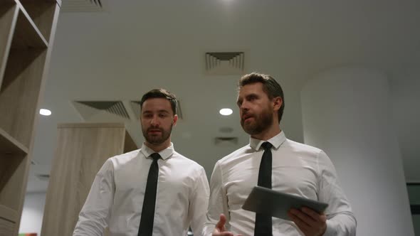 Office Workers Discuss Business Using Digital Tablet Computer in Office Corridor