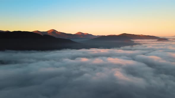 Aerial View of Colorful Sunrise Over White Dense Fog with Distant Dark Silhouettes of Mountain Hills