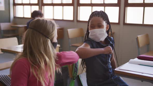 Two girls wearing face masks greeting each other by touching elbows at school