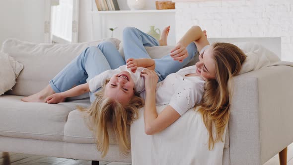Caucasian Young Happy Mother and Little Girl Child Daughter Lie on Couch in Cozy Living Room Spend