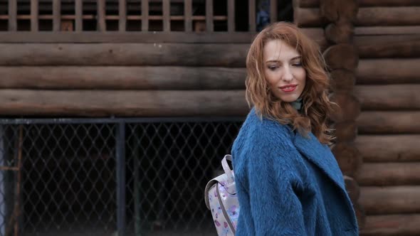 Young Redhaired Woman in a Blue Coat and Walks Against the Backdrop of the Old City