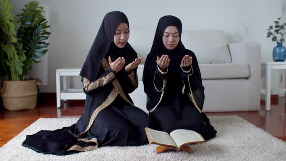 Young Muslim woman and female friend reading Quran and praying