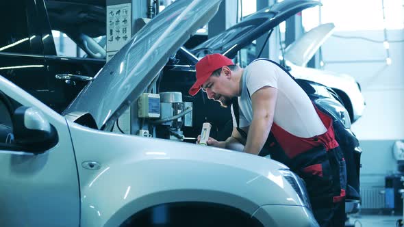 Car Repair Master Checks Under the Hood of a Vehicle with a Flashlight