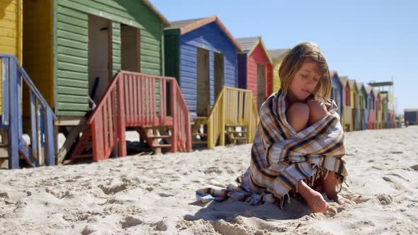 Teenage girl wrapped in blanket playing with sand 