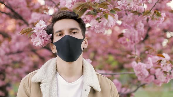 Pandemic, portrait of a young man on a woolen jacket on black virus protective mask on street. 