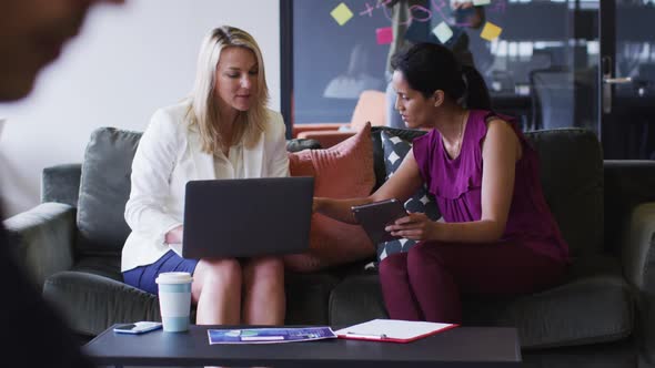 Diverse business people sitting using laptop and digital tablet in office lounge