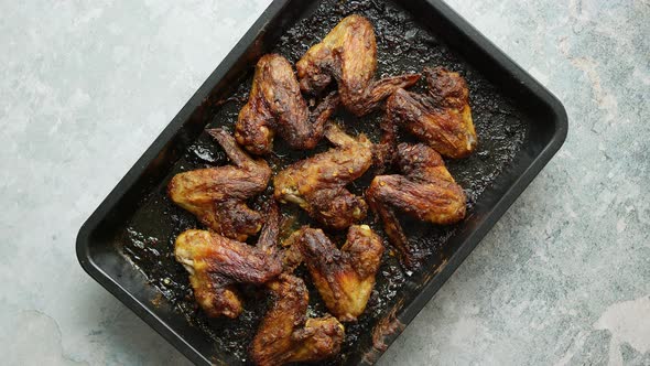 Grilled Chicken Wings in Spices in Black Metal Baking Tray on Stone Table. Top View