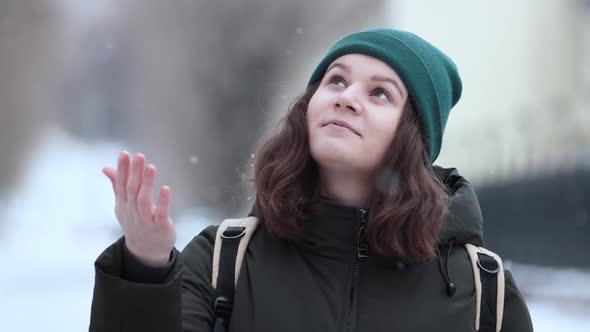 A young woman catches snowflakes with her hand in a snowfall