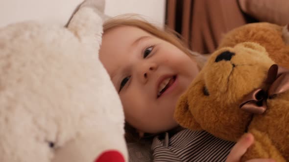 Funny Little Girl Lies in Bed Looking Into Camera Portrait