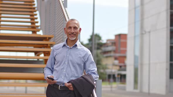 Smiling businessman with smartphone leaning on railing of staircase