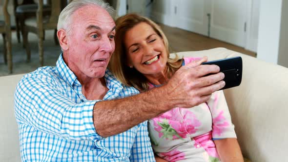 Senior couple taking a selfie on mobile phone in living room