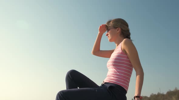 Young Relaxed Woman Sitting Outdoors on a Big Stone Enjoying Warm Summer Day