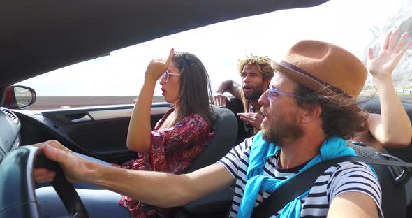 Bearded hipster man driving in convertible on winding motorway with friends