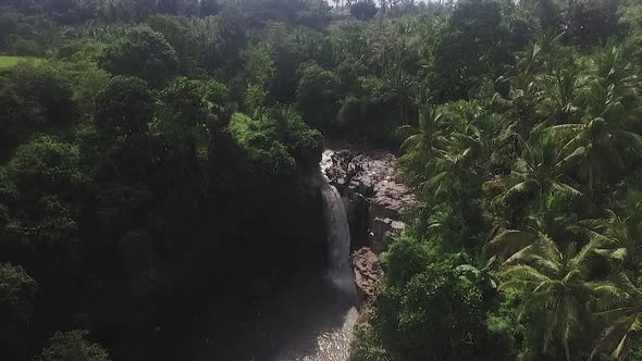 Aerial of Tegenungan Waterfall flowing as tourists enjoy themselves, with greenery surroundings