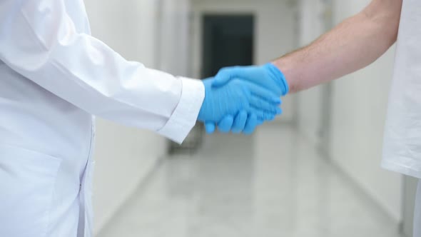 Unrecognizable Man and Woman in Uniform Shaking Hands Standing in Hospital Corridor