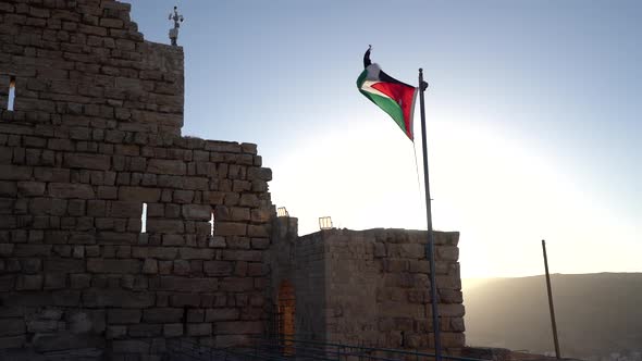 Jordan Flag Waving in the Wind Against Blue Sky and Bright Sun with Old Building in the Background