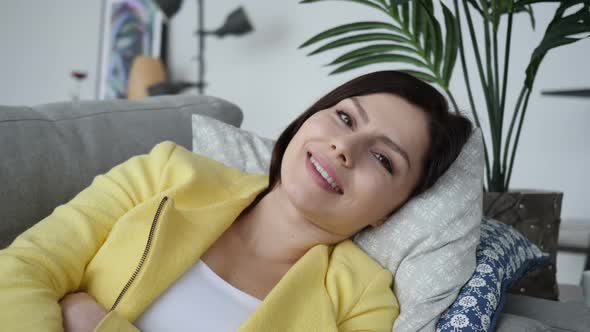 Smiling Young Woman Looking at Camera While Laying on Sofa at Home