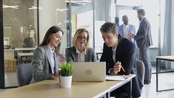 Three Office Workers Business Colleagues Sitting at Desk and Discussing Work