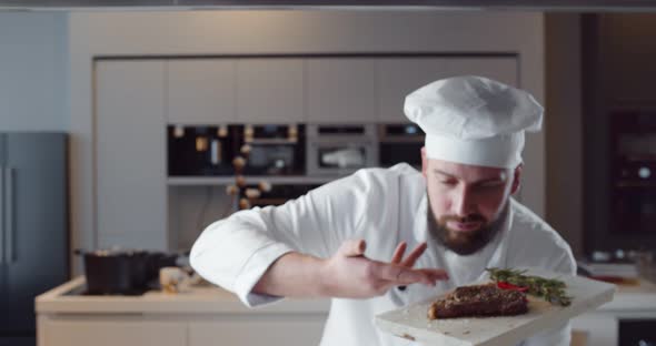 Young Handsome Chef in White Uniform Holding Wooden Board with Ready Beef Steak