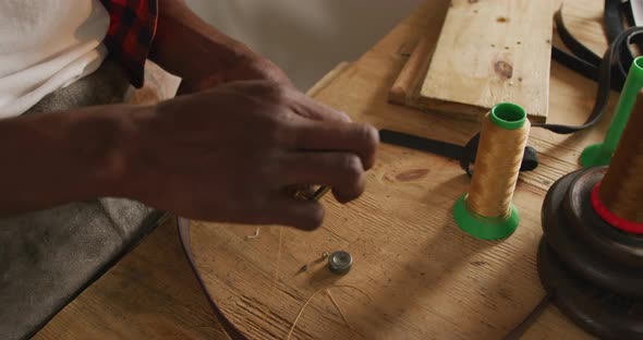 Hands of african american craftsman using tools to make a belt in leather workshop