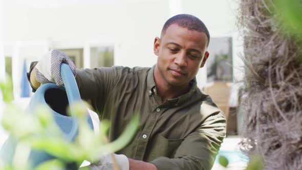 Portrait of biracial man gardening, watering plants with watering can