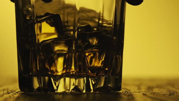 Whiskey with Ice Cubes Rotating in Glass. Hand Holds Glass with Golden Whisky