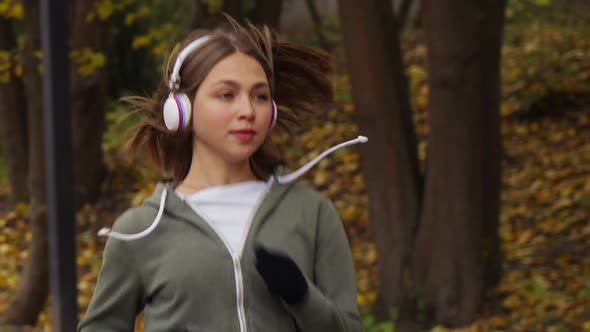 Woman with headphones jogging in nature on autumn day