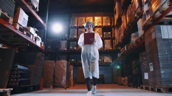 Pretty Young Lady Walking Between Shelves in Huge Storage Room and Making Notes During Inspection in