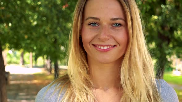 Young Pretty Blond Woman Shows Thumb Up on Agreement - Park with Trees in Background - Closeup