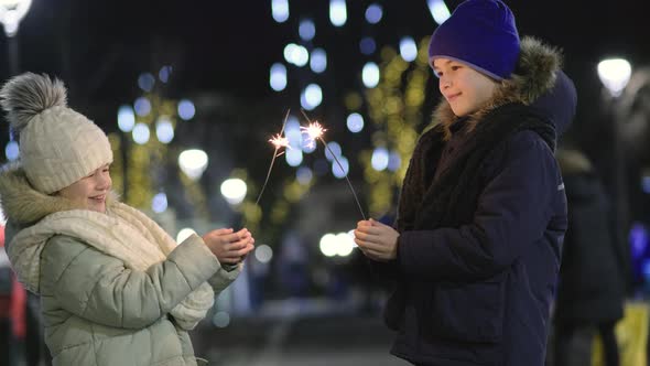 Two cute young children, boy and girl in warm winter clothing holding burning sparkler fireworks