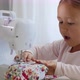 A Little Girl Is Sewing Fabric and Talking. Mom Is at the Background. Close-up. - VideoHive Item for Sale