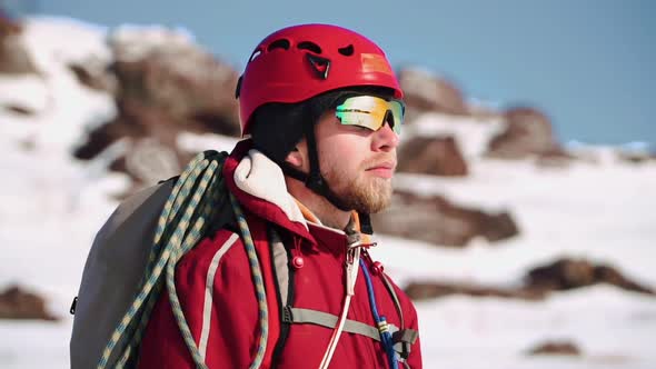 Young Climber of Caucasian Appearance with a Beard Standing on a Snow Slope and Looks Into the