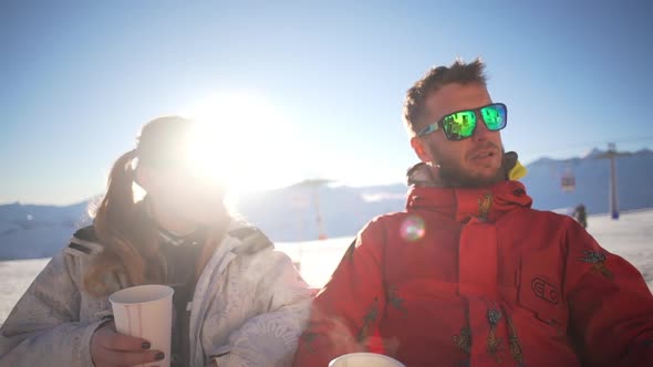 Caucasian Male Witn Beard and Mirrow Glasses Sitting and Talking with Female in Ski Mountain Resort