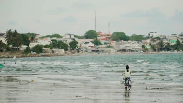 Little girl rides bicycle on Vietnamese seashore of Mui Ne beach, near fisherman village