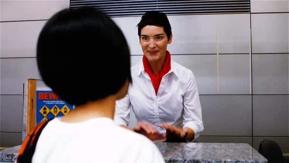 Female airport staff checking passport and interacting with woman at check-in desk