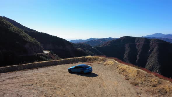 Flying slowly towards mountains and over a blue Tesla Model S on Mt. Baldy in Southern California.