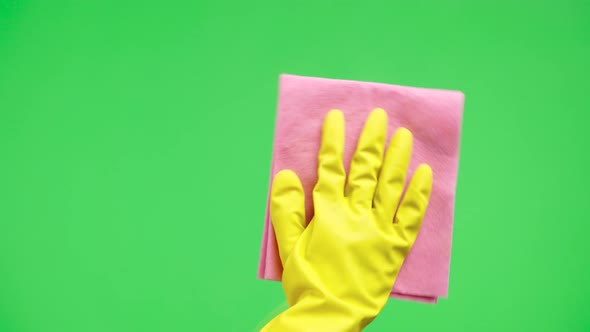 Woman's Hand in Yellow Rubber Gloves Wipes Window Glass with Dry Rag Against the Background of Green