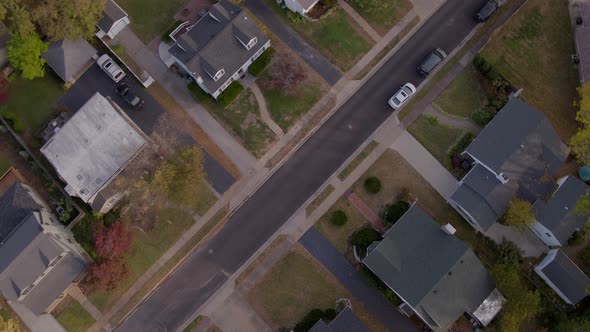 Drone camera spins and descends down towards an autumn suburban street below