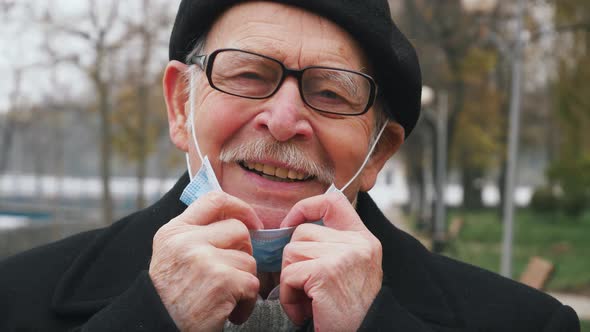 elderly man takes off medical mask. Breathes deeply and smiling looking at camera on blurred backgro