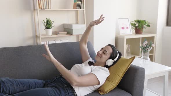 Happy Young Adult Woman Listening to Music and Dancing While Relaxing at Home